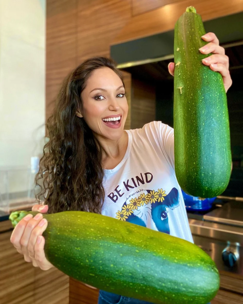 Cheryl showing off two enormous zucchinis in her kitchen